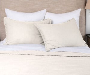 Bed with white and beige pillows and a cream blanket in a neutral toned bedroom