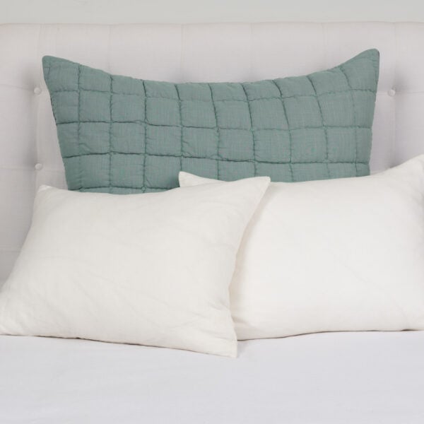 Bed with white linens and a large teal quilted pillow flanked by nightstands with vases and books on either side