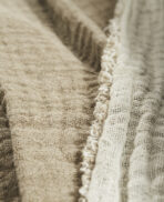 Close up of beige burlap fabric with a woven texture and frayed fringe along the edge highlighting rough fibers