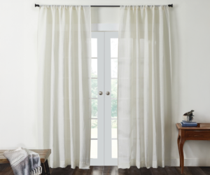 White sheer curtains frame glass french doors with a bench and a throw on the left and a small wooden table with a plant on the right