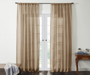 Beige sheer curtains framing white french doors with a throw blanket on a bench to the left and a wooden table with books on the right