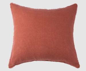 Orange red square throw pillow with frayed edges set against a light background