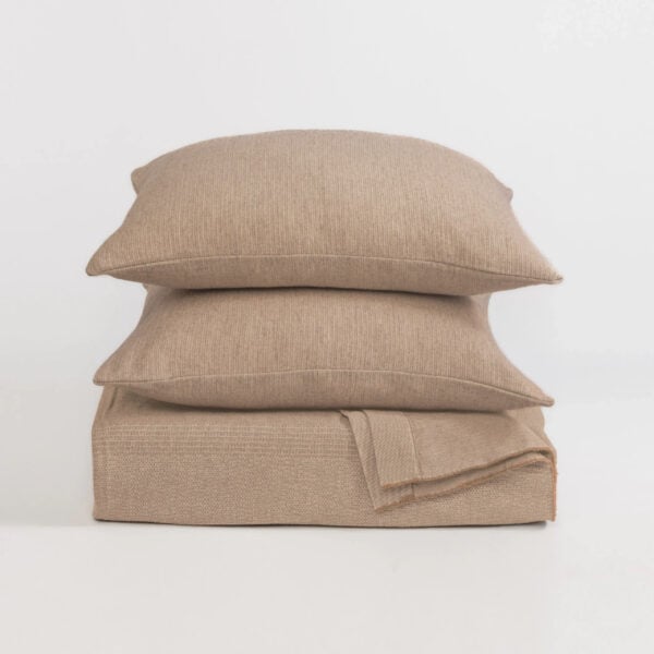Stack of beige knit pillows on a white background, arranged in a vertical pile.