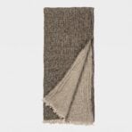 Brown woven scarf with light fringe along the bottom edge hanging vertically against a pale background