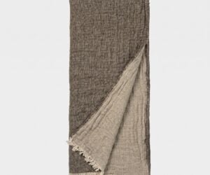 Brown woven scarf with light fringe along the bottom edge hanging vertically against a pale background