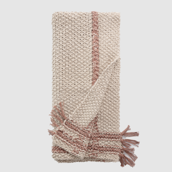 Beige woven throw blanket with a pink decorative stripe and fringed ends folded diagonally