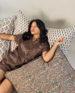 Woman lying on a patterned sofa or bed resting among floral cushions in brown striped pajamas looking to the side