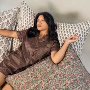 Woman lying on a patterned sofa or bed resting among floral cushions in brown striped pajamas looking to the side