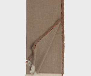 Beige herringbone throw blanket with fringed edges folded to reveal a red stitched border and tassels at the corner