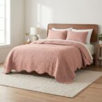 Bedroom with a wooden headboard bed blush pink quilt and pillows white sheets and a bedside lamp on a small nightstand