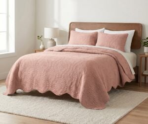Bedroom with a wooden headboard bed blush pink quilt and pillows white sheets and a bedside lamp on a small nightstand