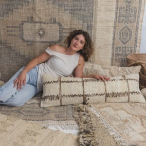 Young woman with curly hair lying down on a layered beige and blue woven rug setup modeling casually
