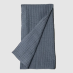 Blue gray waffle knit blanket folded with one corner pulled over the edge on a light background