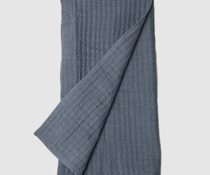 Blue gray waffle knit blanket folded with one corner pulled over the edge on a light background