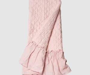 Pink quilted blanket with diamond stitching and a gathered ruffle at the edge folded throwblanket