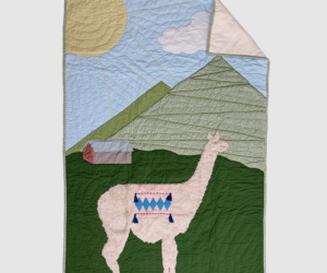 Quilted wall hanging showing a pink llama in a green valley with mountains sun and a small house in the background