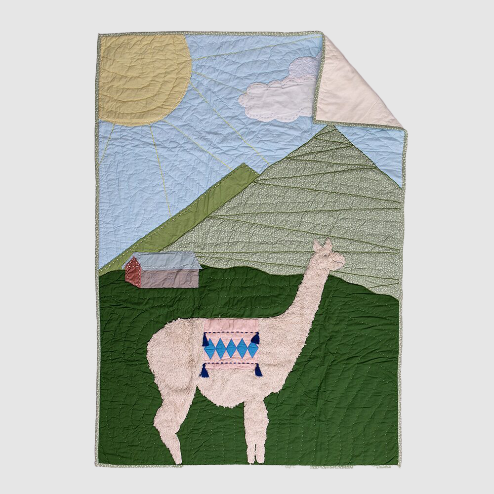 Cc1010b | Amity Home Quilted wall hanging showing a pink llama in a green valley with mountains sun and a small house in the background