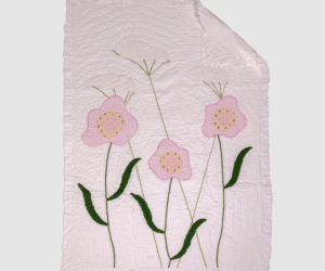 Light pink quiltthrow with embroidered pink flowers and green stems along the edges decorative ruffled border