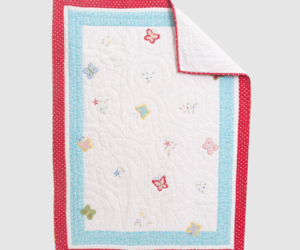 Quilted blanket with white center butterfly pattern and red and blue polka dot borders folded at corner for display