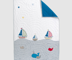 Whimsical nautical quilt with sailboats whales and striped waves on white fabric blue corner folded back in a child friendly scene