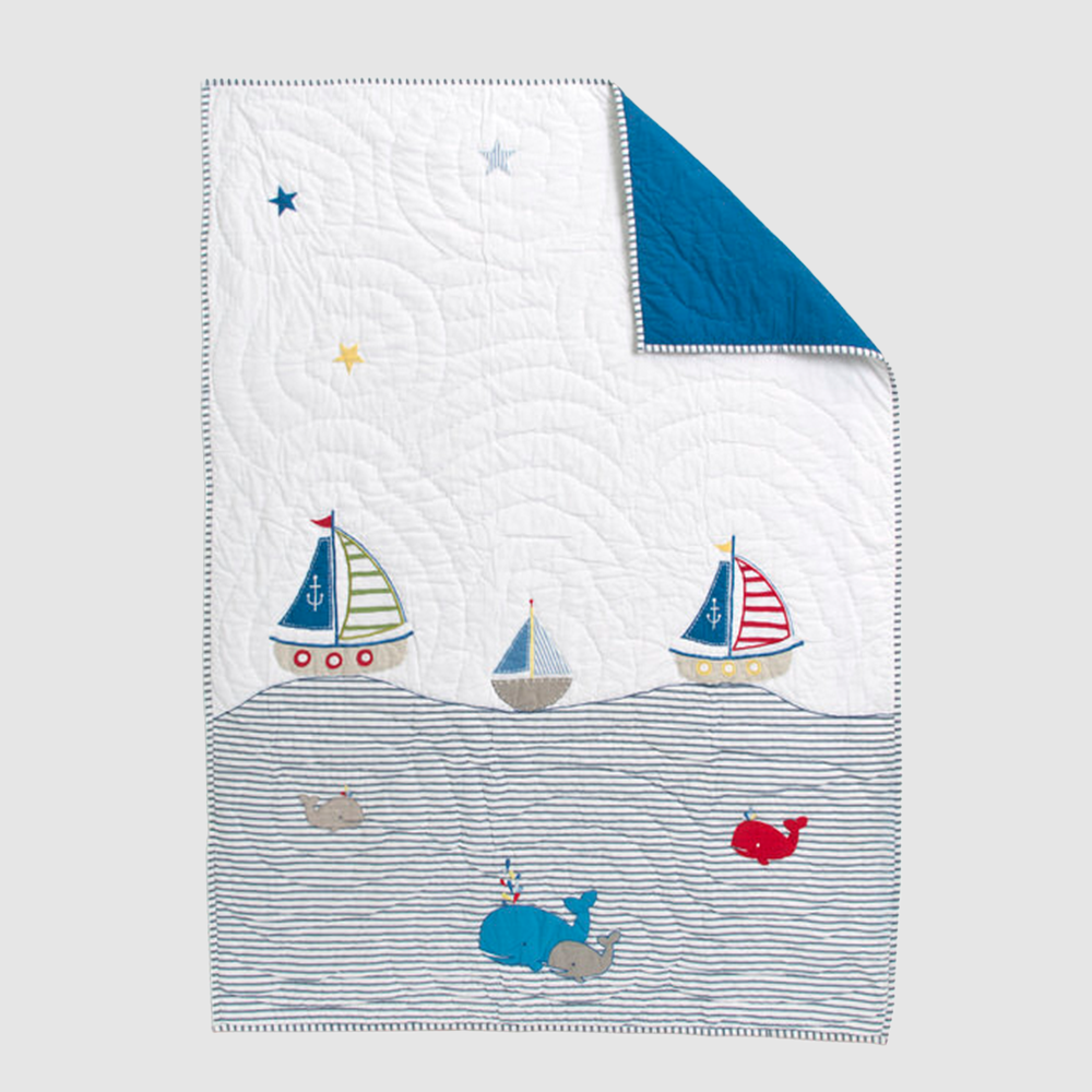 Cc805 | Amity Home Whimsical nautical quilt with sailboats whales and striped waves on white fabric blue corner folded back in a child friendly scene