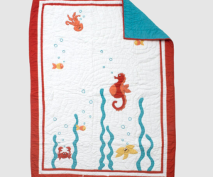 White quilted baby blanket with a red border featuring a seahorse fish and crab among blue seaweed one corner folded back to reveal a turquoise underside