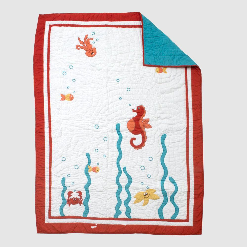 Cc886 | Amity Home White quilted baby blanket with a red border featuring a seahorse fish and crab among blue seaweed one corner folded back to reveal a turquoise underside