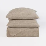 Stack of beige knitted cushions stacked against a white background