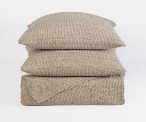 Stack of beige knitted cushions stacked against a white background