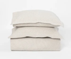 Stack of three cream colored pillows with a subtle geometric pattern on a white background