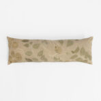Beige decorative pillow with a green leafy botanical pattern against a white background