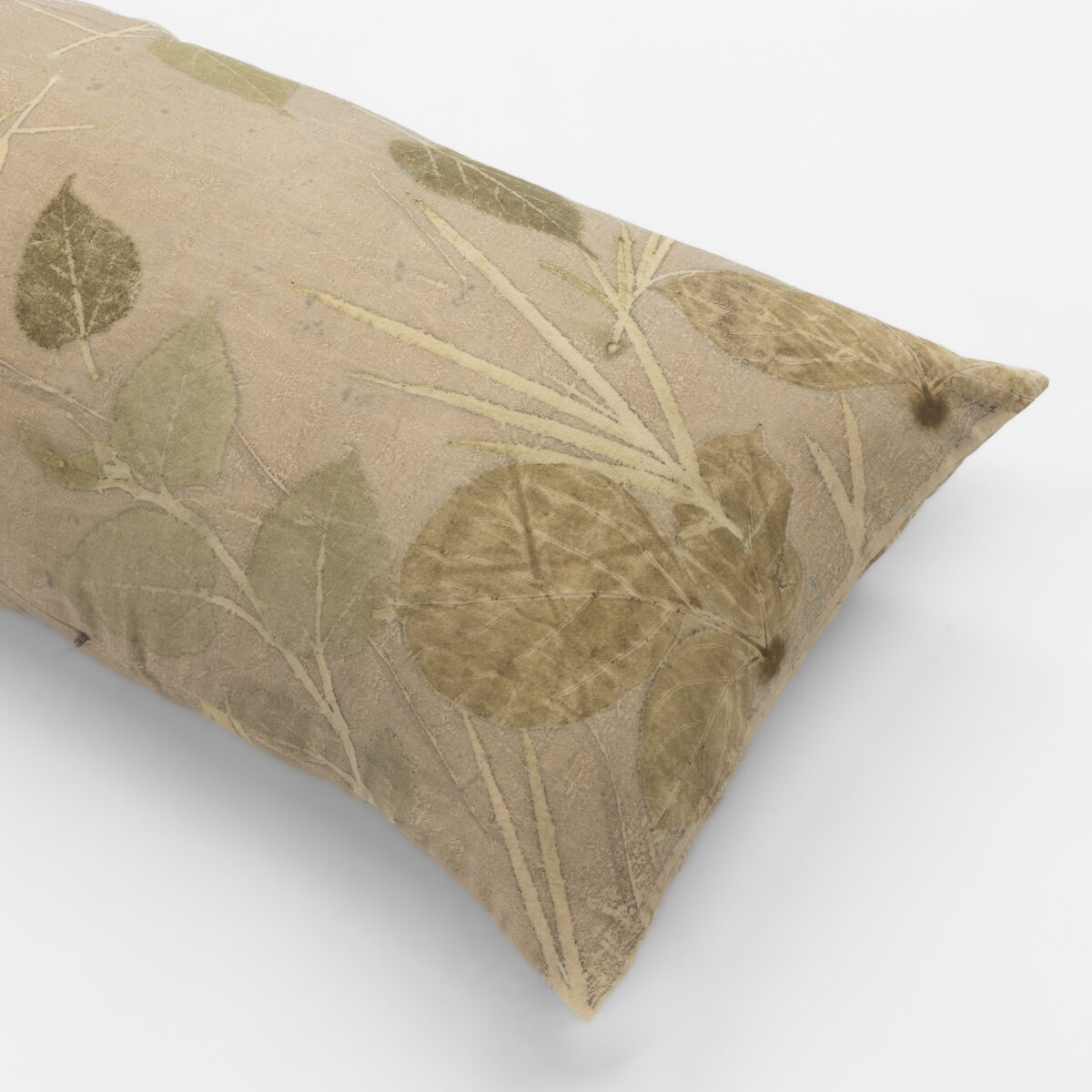 Beige fabric pillow with a green botanical leaf pattern on a white background close up view