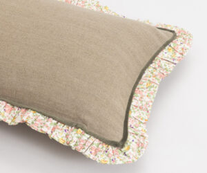 Close up of stacked burlap front cushions with floral printed ruffled edges showing pink yellow and green floral pattern