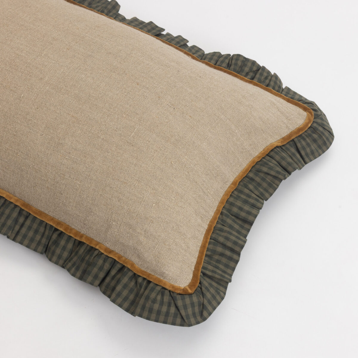 Beige burlap cushion with brown piping resting on a dark green plaid pillow