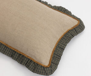 Beige burlap cushion with brown piping resting on a dark green plaid pillow