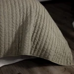Close up of a cream quilt with vertical quilting stitches laid on a wooden floor surface