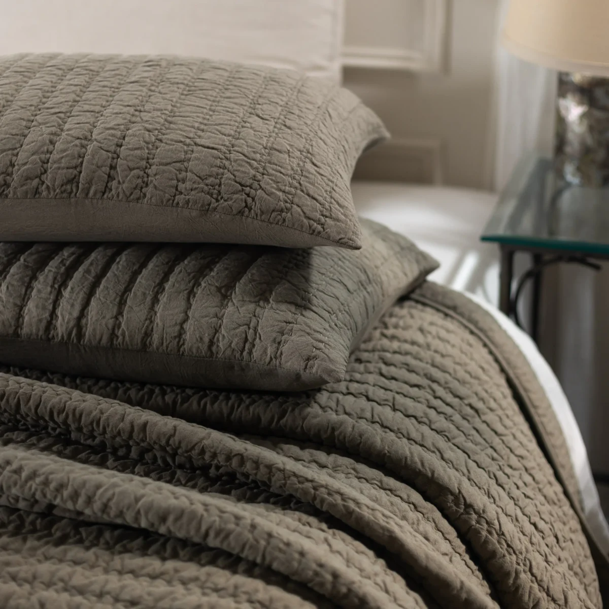 Close up of gray quilted blankets stacked on a bed highlighting textured stitching and folds