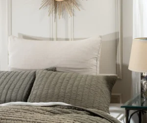 Gray quilted bedspread with a white pillow and a gold sunburst mirror on the wall above the headboard creating a luxe bedroom detail