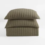 Stack of three beige quilted pillows with vertical stitching on a white background