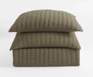 Stack of three beige quilted pillows with vertical stitching on a white background