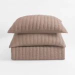 Close up of a quilted beige pillow stacked on other pillows against a white background showing textured stitching