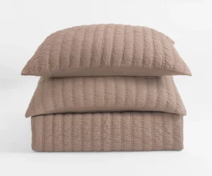 Close up of a quilted beige pillow stacked on other pillows against a white background showing textured stitching