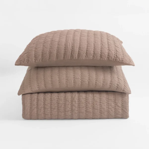 Close-up of a quilted beige pillow stacked on other pillows against a white background, showing textured stitching.