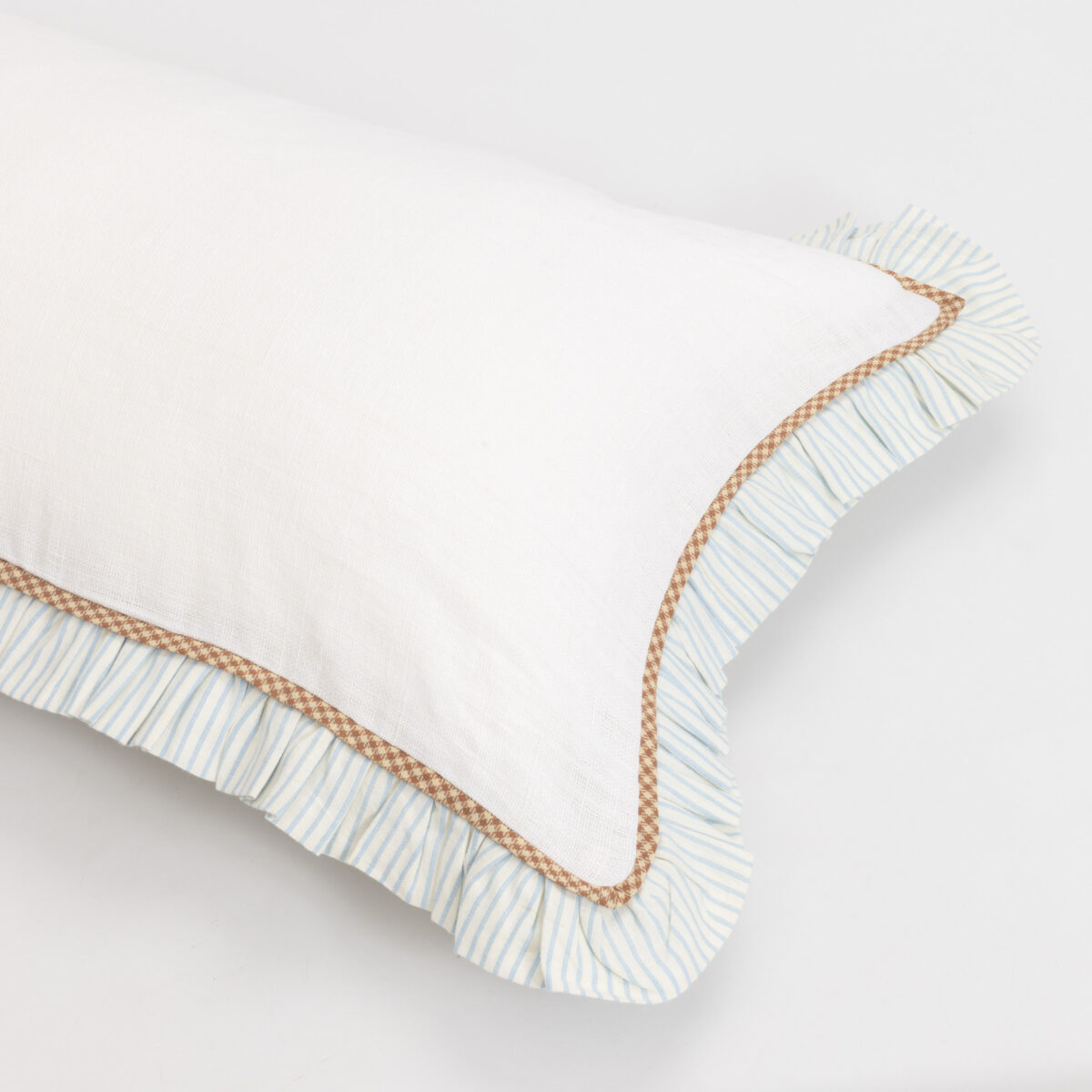 Close up of a white pillow with a blue striped pillow underneath and brown trim along the edge showing overlapping fabrics