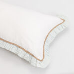 Close up of a white pillow with a blue striped pillow underneath and brown trim along the edge showing overlapping fabrics