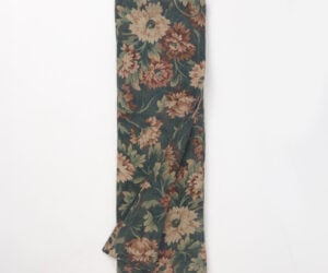 Folded length of dark green floral fabric with tan and dusty rose flowers viewed from above showing a textile swatch