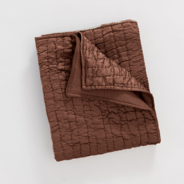 Close up of a brown quilted fabric with square stitching folded on a light background