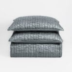 Stack of three textured gray quilted pillows on a white background viewed from the side edge of the top pillow edge