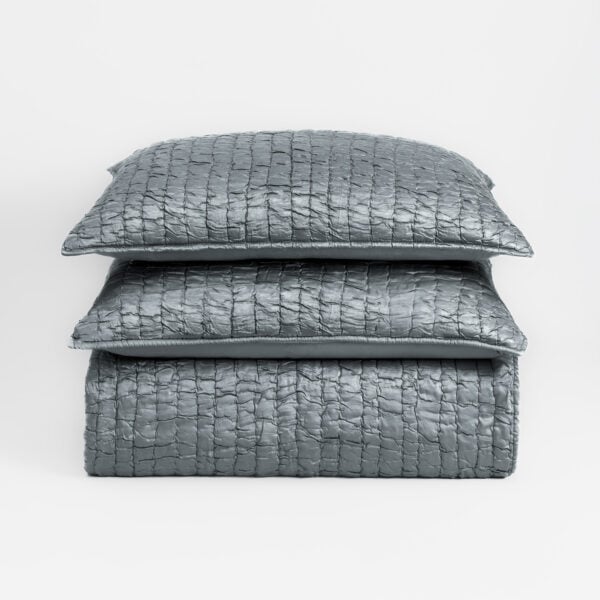 Stack of three textured gray quilted pillows on a white background, viewed from the side edge of the top pillow edge.