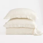 Three white pillows stacked on top of each other with ruffled edges against a white background